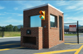 A compact prefabricated security booth with large windows and an enclosed workspace for monitoring vehicles and visitors at a school entrance.