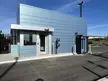 Exterior view of a 16' x 34' pre-assembled steel guardhouse installed at a parking lot entrance, featuring blue ACM panel cladding, large tinted windows, multiple access doors, and a parapet roof designed for security and access control operations.